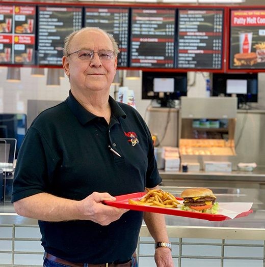 Henry Rice smiling in a Bronco's shirt, holding a red tray with a burger and fries